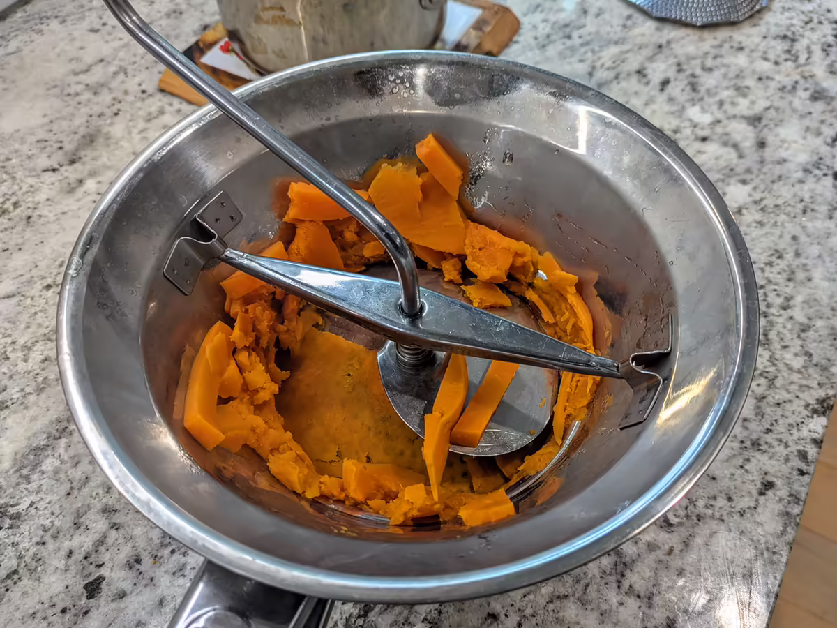 vintage metal ricer with chunks of boiled sweet potatoes in the process of being riced